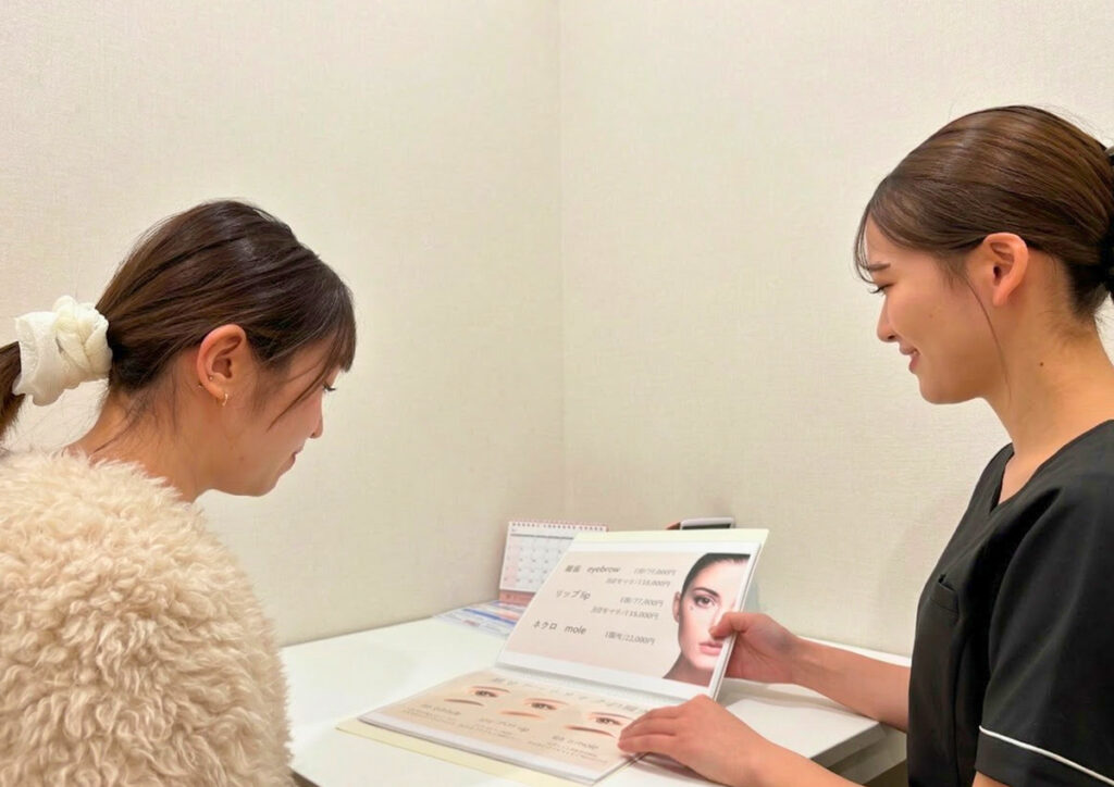 スタッフが、アートメイクのメニューカタログを開きながら顧客にカウンセリングを行っている
