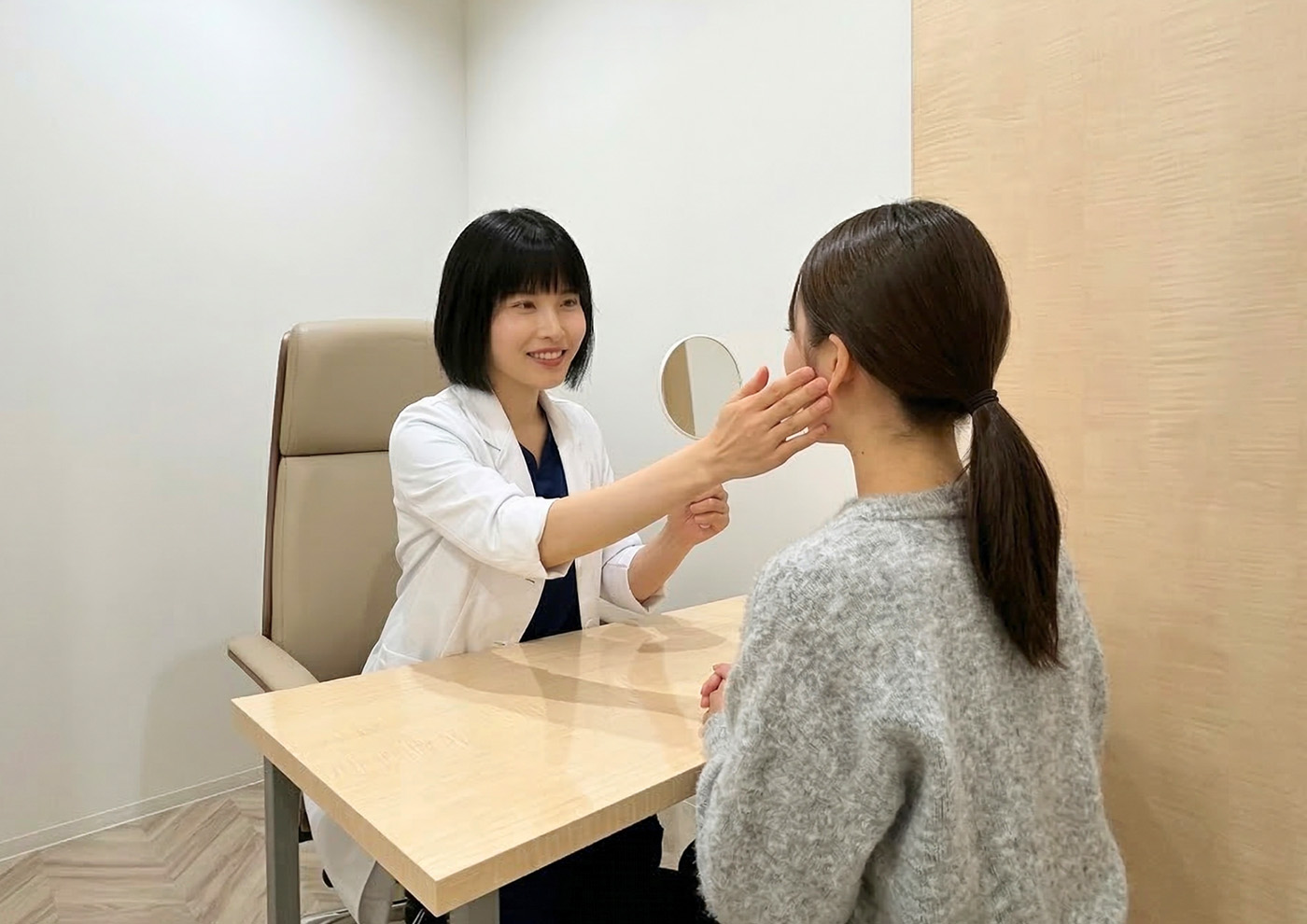 白衣を着た女性医師が診察室で患者の顔に触れながら肌の状態を確認している