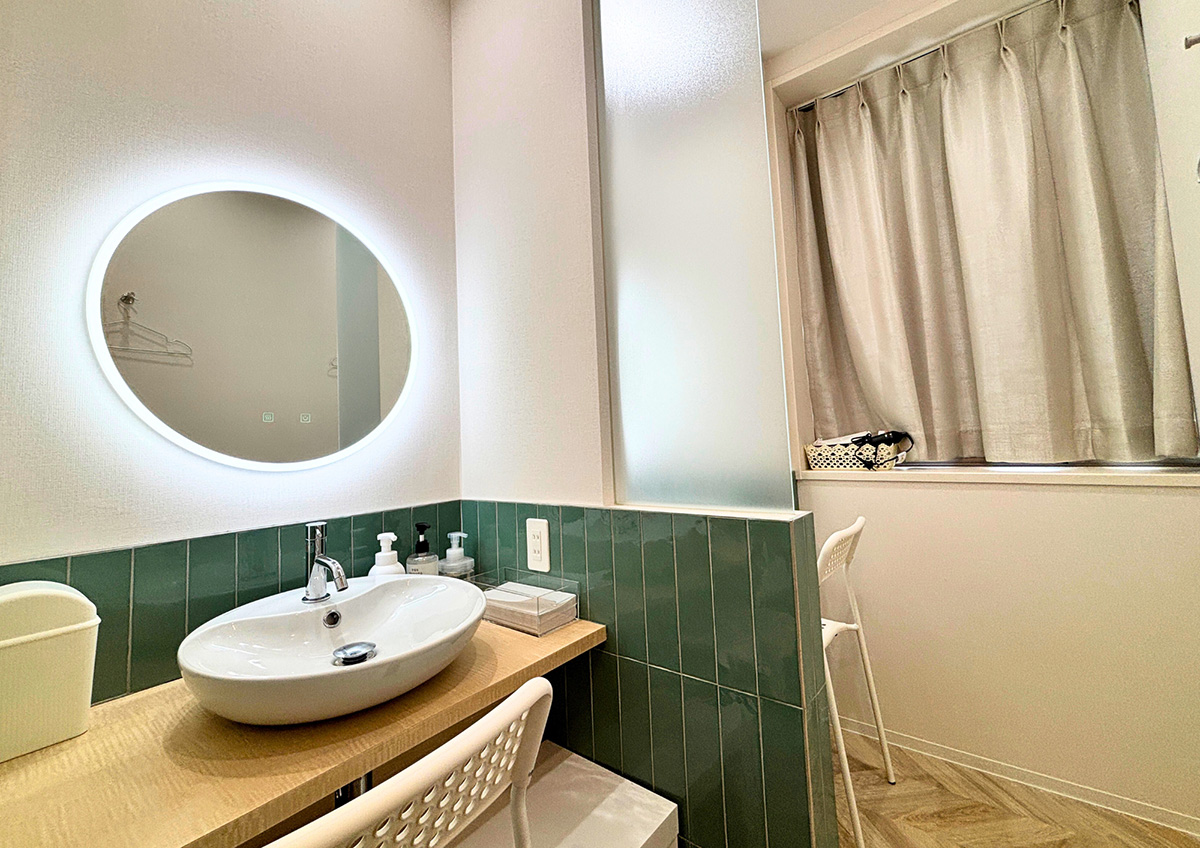 グリーンタイルの壁とLEDバックライト付き丸型ミラーを備えたパウダールーム
