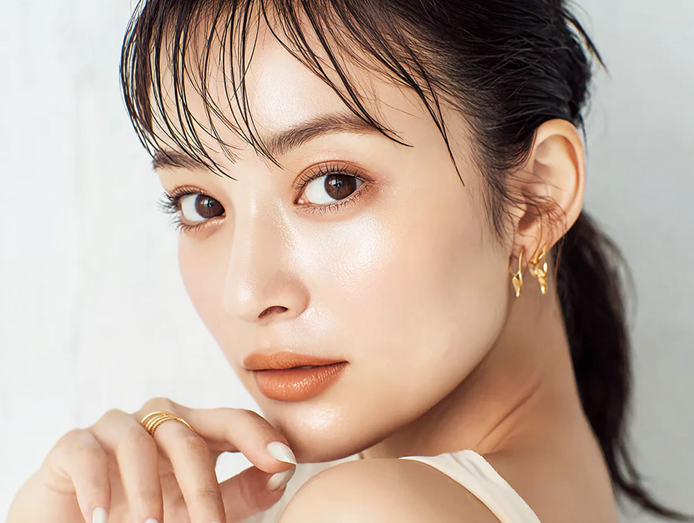 透明感のあるツヤ肌の女性がカメラを見つめ、顎に手を添えているクローズアップポートレート