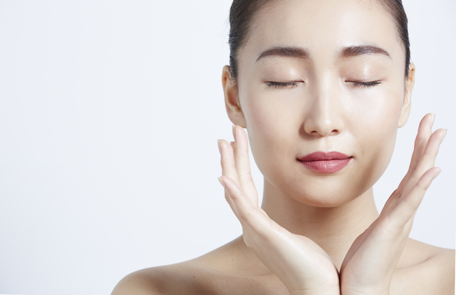 目を閉じて両手を頬に添える女性。透明感のある肌とリラックスした表情