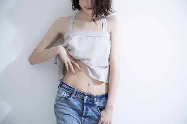 白いタンクトップとデニムを着た女性が、腹部を手で押さえている様子